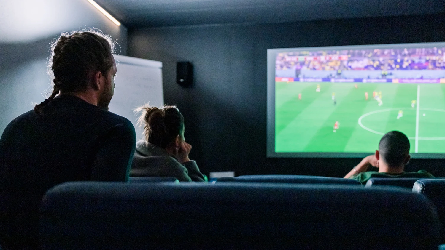 Jeunes apprentis regardant un match de foot dans une salle de cinéma.