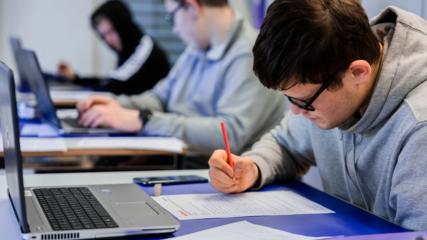 Trois jeunes apprentis qui étudient devant leurs ordinateurs, l'un d'eux écrit sur une feuille.